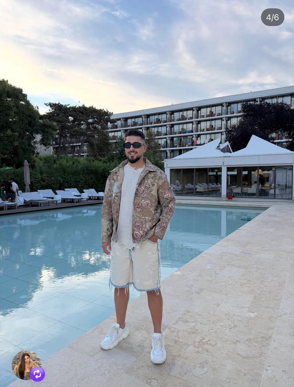 Patrick wearing a tapestry jacket and white shorts beside a pool